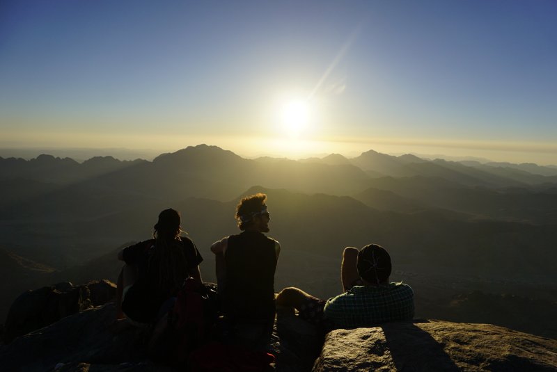 The sun is low on the horizon, casting a warm golden light across the sky and creating long shadows.

The people are seen from behind, suggesting a calm, reflective moment rather than action.